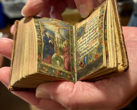 A little illuminated incunable book of hours in the palm of my hand, opened to a crucifixion scene.