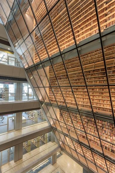 A large multistory atrium of bookshelves enclosed in a glass wall that angles out as it rises.
