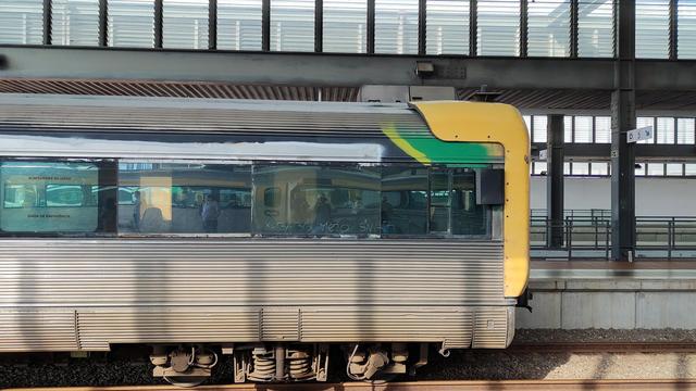The power car of a Portuguese CP Suburbano train. The body is made of stainless steel, the driver cabin is surrounded by yellow plastic elements. The train is standing inside a station.